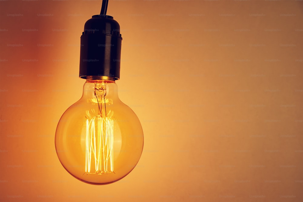 Vintage light bulb on orange background with copy space. Glowing edison bulb