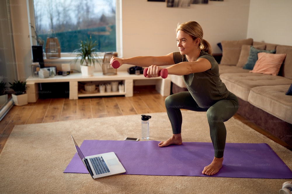Athletic woman using hands weights while practicing squats in the living room.