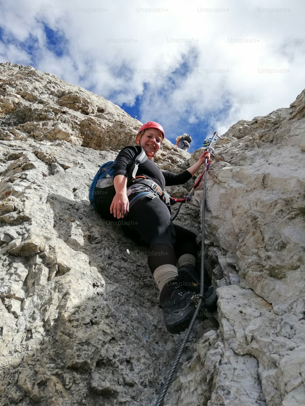 Vista vertical de una atractiva escaladora rubia en una empinada vía ferrata en los Dolomitas italianos con una gran vista detrás
