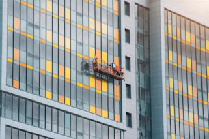 A construction team in a suspended cradle on cables is working on the facade of the building
