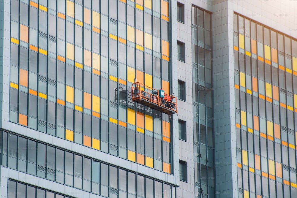 A construction team in a suspended cradle on cables is working on the facade of the building