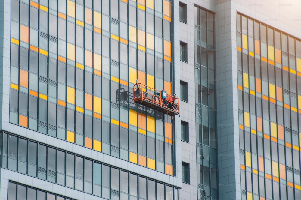 Ein Bauteam in einer aufgehängten Wiege an Kabeln arbeitet an der Fassade des Gebäudes