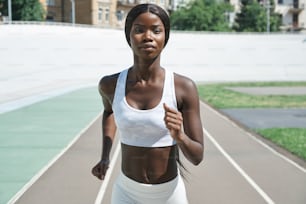 야외에서 트랙을 달리�는 스포츠 의류를 입은 아름다운 젊은 아프리카 여성