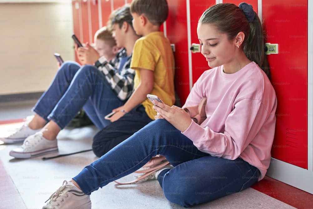 Schülerinnen und Schüler sitzen mit dem Smartphone
