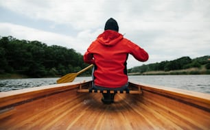 湖でカヌーを漕ぐ男性の後ろ姿。雨の日のボートに乗る。
