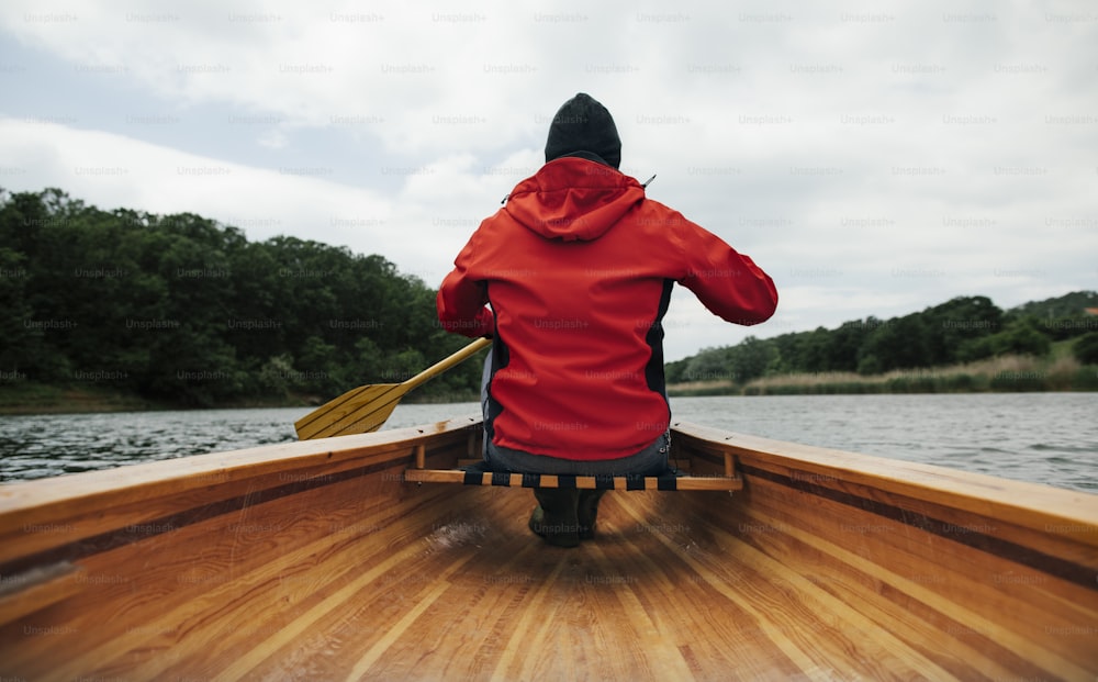 Vista trasera de un hombre remando en canoa en el lago. Paseo en barco para días lluviosos.