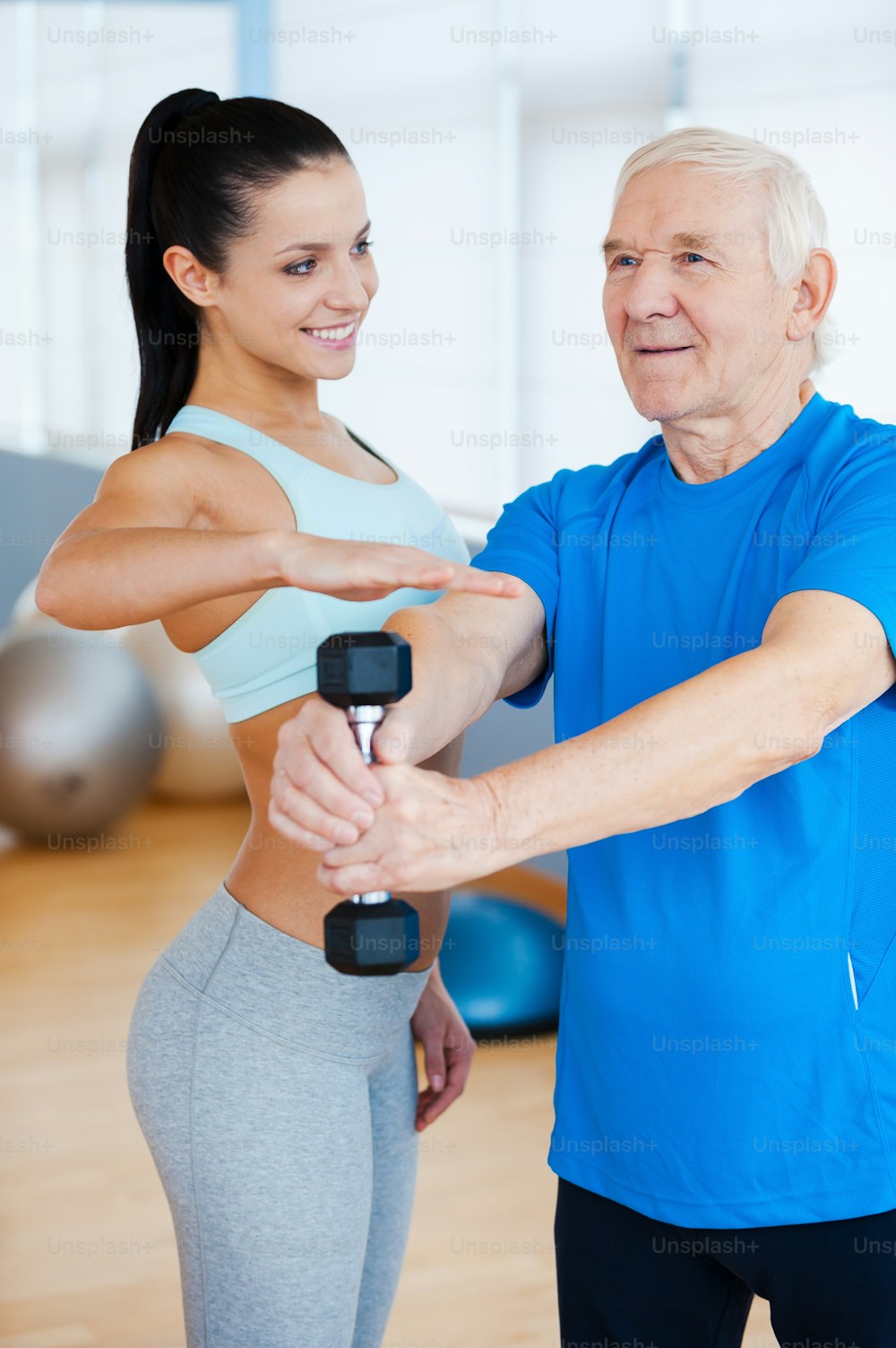 Confident female physical therapist helping senior man with fitness in health club