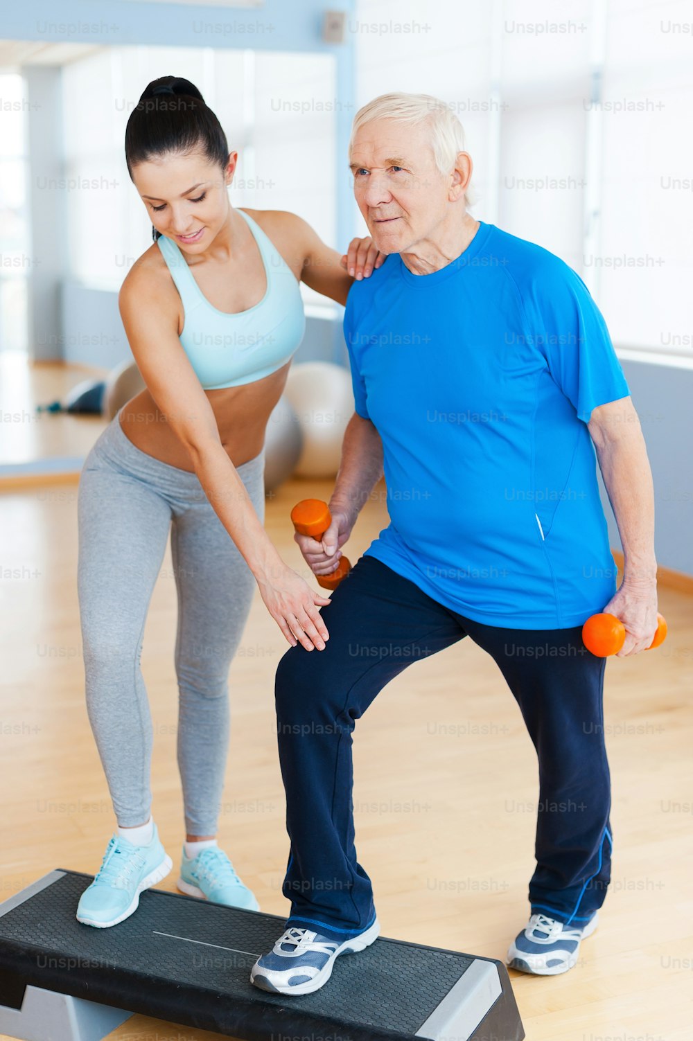 Full length of confident female physical therapist working with senior man in health club