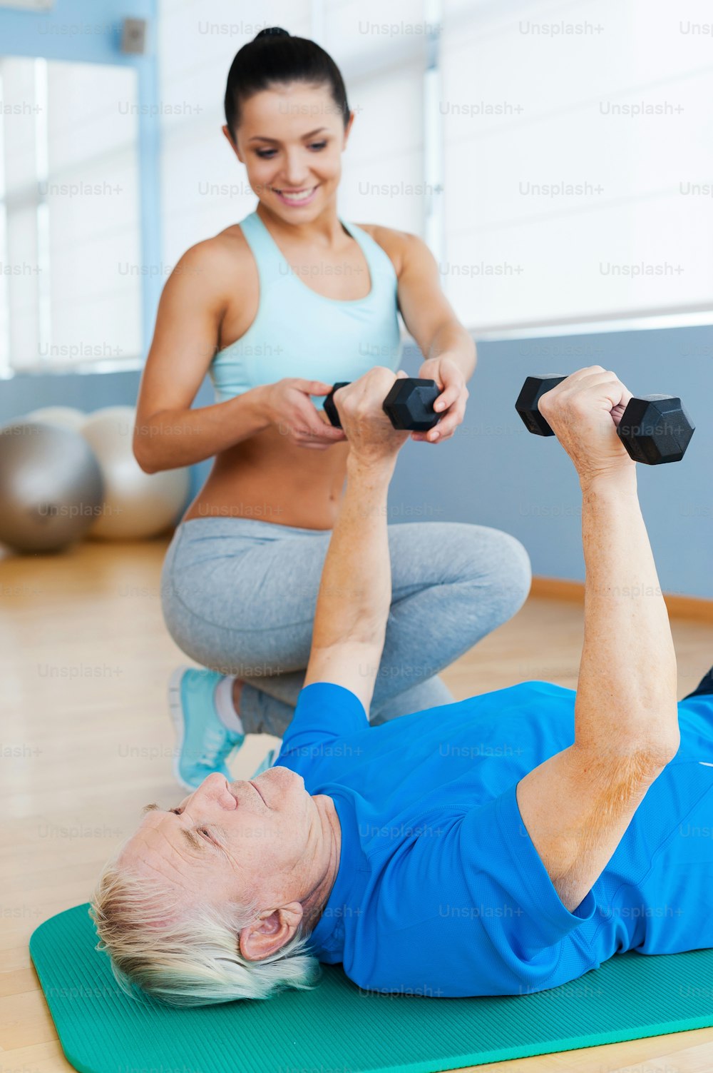Confident female physical therapist supporting senior man in weight exercises