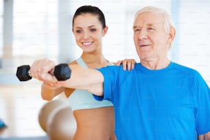 Cheerful female physical therapist helping senior man with fitness in health club