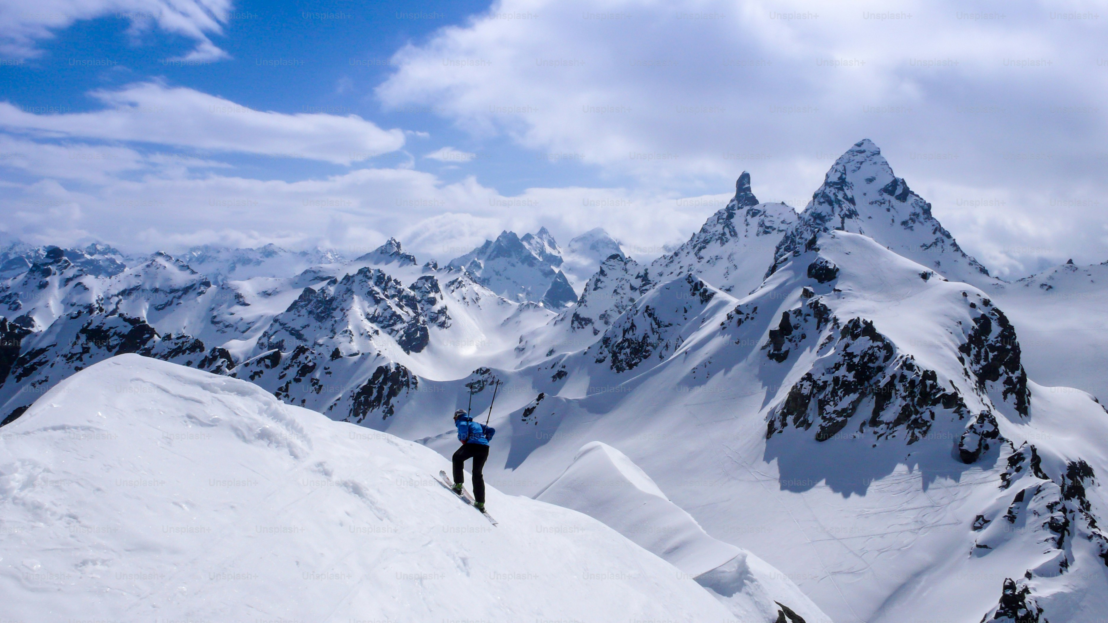male backcountry skier skiing down from a high peak in the backcountry of the Swiss Alps on a ski tour in winter with a fantastic view and acting a bit silly