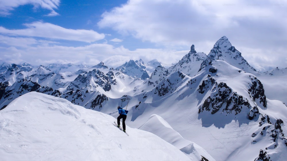 männlicher Backcountry-Skifahrer, der im Winter auf einer Skitour mit fantastischer Aussicht von einem hohen Gipfel im Hinterland der Schweizer Alpen abfährt und sich ein bisschen albern benimmt
