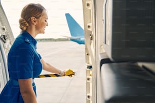 Smiling contented attractive flight attendant in leather gloves closing the airplane entrance with a barrier tape