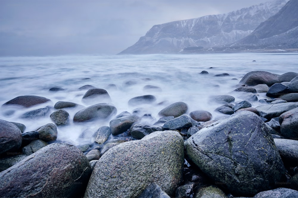 冬の嵐の中、ノルウェーのロフォーテン諸島にあるウンスタッドビーチの石の岩に押し寄せるノルウェー海の波。長時間露光