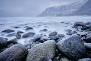 Olas del mar noruego que se levantan sobre las rocas de piedra en la playa de Unstad, islas Lofoten, Noruega en una tormenta de invierno. Larga exposición