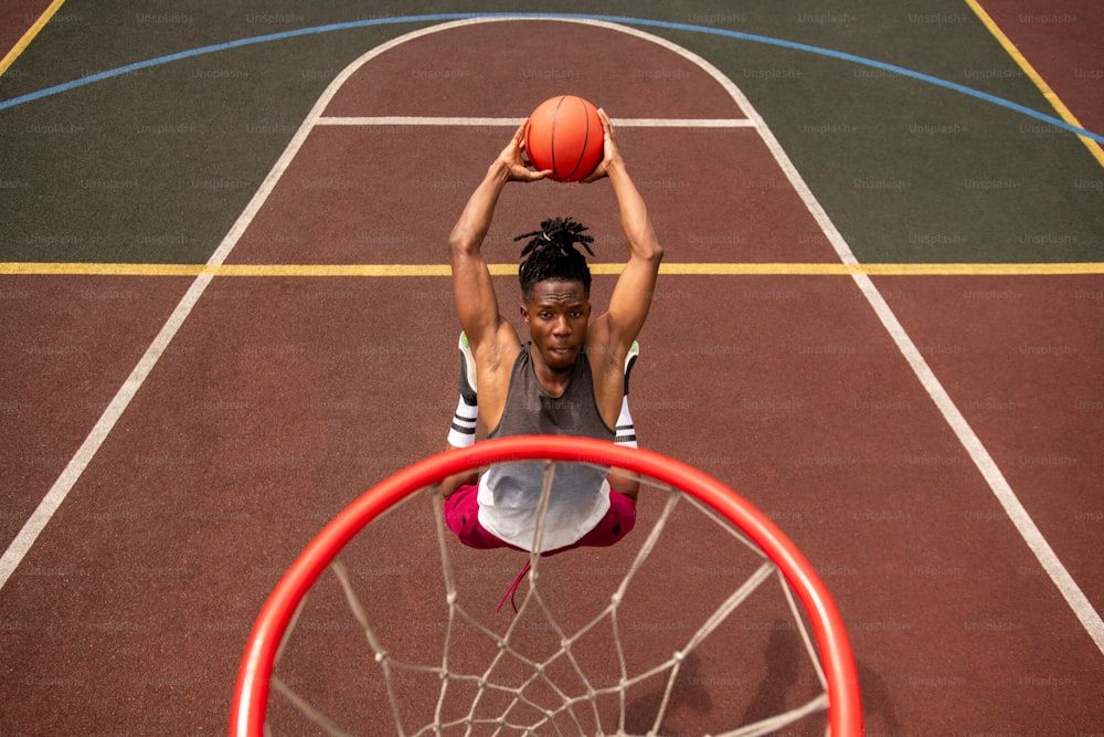 African young basketball player making effort while jumping and throwing ball in basket during training