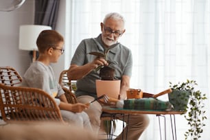 Senior man teaching his grandson about repotting houseplants at home.