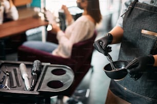 Close-up of hairdresser preparing dye in a container at hair salon.