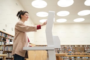 Jeune femme utilisant un équipement spécial et choisissant un livre dans la bibliothèque