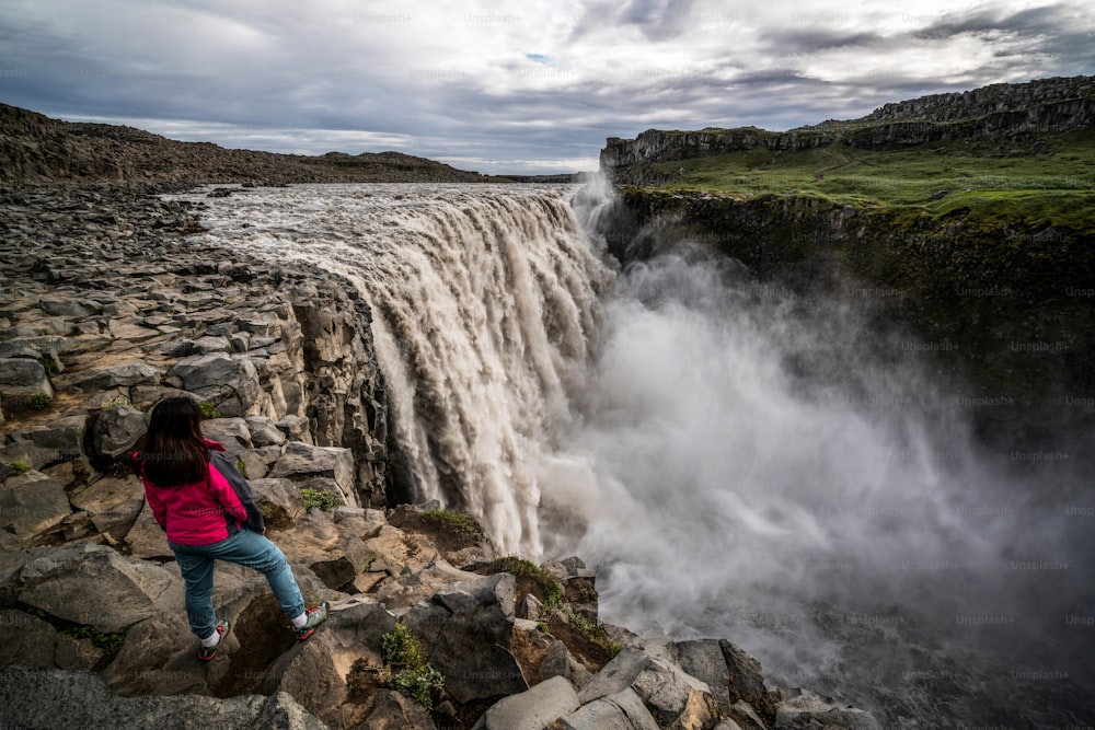Donna viaggiatrice al sorprendente paesaggio islandese della cascata di Dettifoss nel nord-est dell'Islanda. Dettifoss è una cascata nel Parco Nazionale di Vatnajokull, considerata la cascata più potente d'Europa.