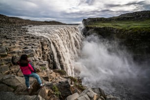 Donna viaggiatrice al sorprendente paesaggio islandese della cascata di Dettifoss nel nord-est dell'Islanda. Dettifoss è una cascata nel Parco Nazionale di Vatnajokull, considerata la cascata più potente d'Europa.