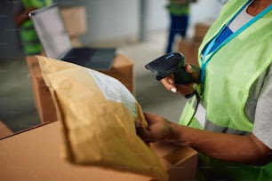 Gros plan d’un employé d’entrepôt scannant l’étiquette sur les colis dans le compartiment de distribution.