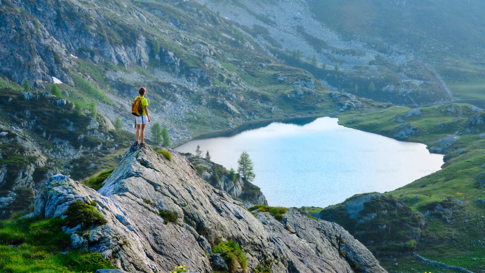 La muchacha mira el lago de la montaña durante un trekking de montaña