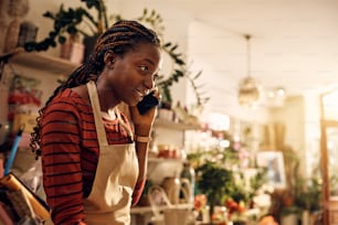 Young African American florist communicating over smart phone while working at her flower shop.