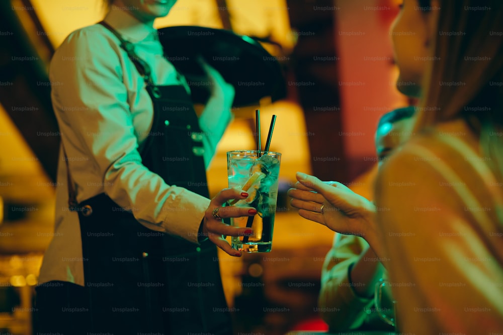 Primer plano de la camarera sirviendo bebidas a los invitados en un pub por la noche.