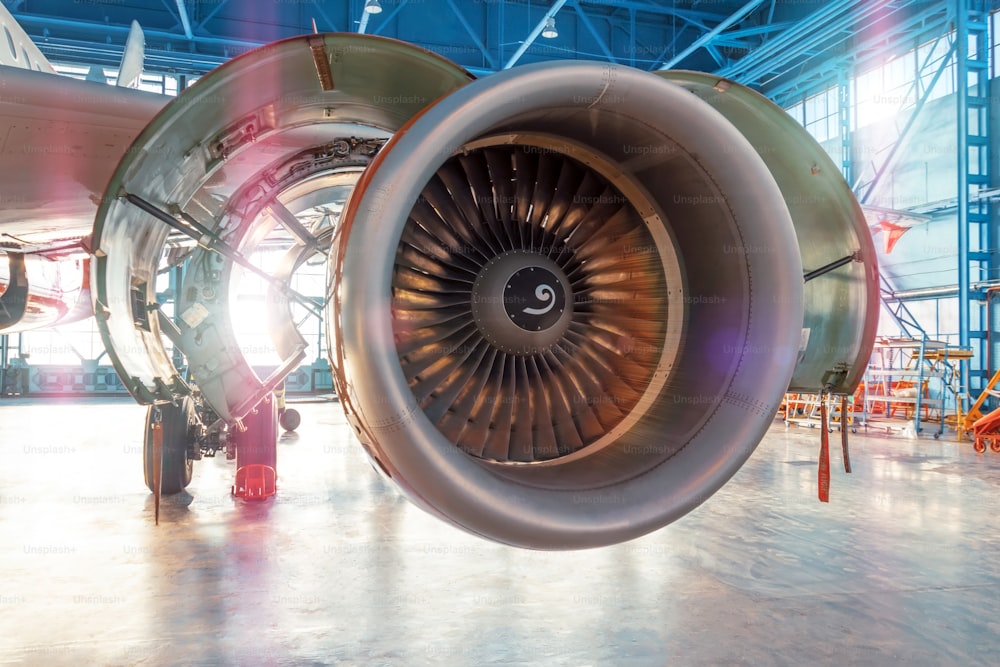 Industrial view of an airplane engine with an open hood for repair in aviation hangar, with bright light outside the gate