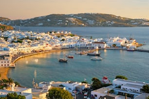 Vista da cidade de Mykonos destino de férias turísticas gregas com famosos moinhos de vento e porto com barcos e pôr do sol yachtson. Mykonos, Ilhas Cíclades, Grécia. Com movimento panorâmico horizontal da câmera