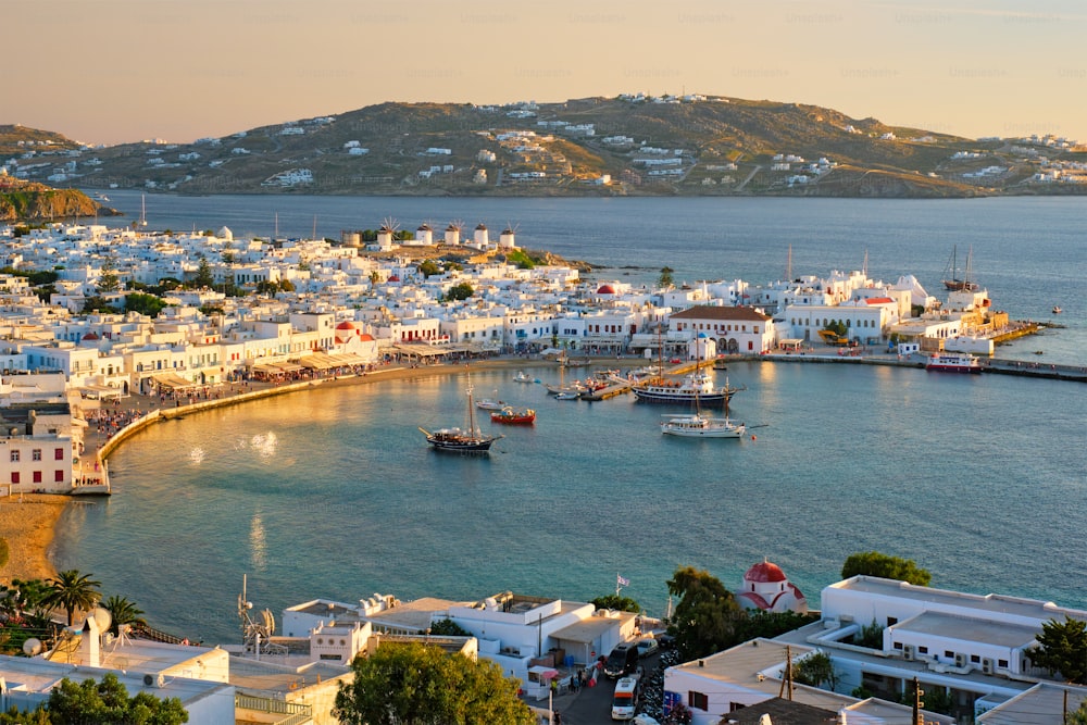 Vue de la ville de Mykonos, destination de vacances touristique grecque avec des moulins à vent célèbres, et le port avec des bateaux et des yachts au coucher du soleil. Mykonos, îles des Cyclades, Grèce. Avec panoramique horizontal de la caméra