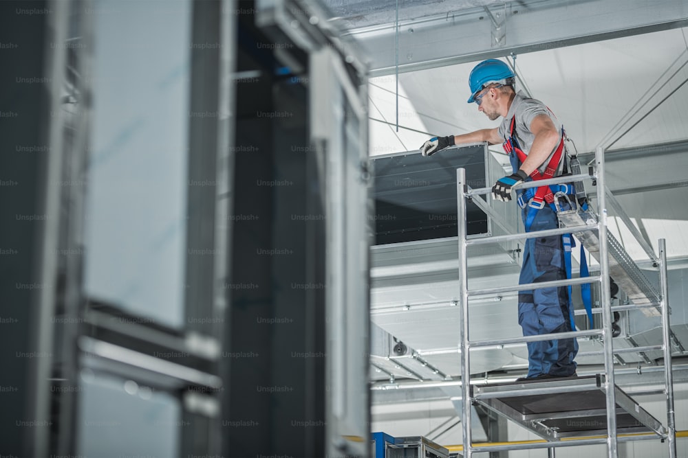 대형 상업용 건물의 천장에 새로 설치된 공기 환기 샤프트를 확인하는 건설 노동자.