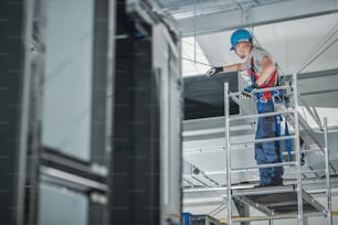 Construction Worker Checking Newly Installed Air Ventilation Shaft On Ceiling Of Large Commercial Building.