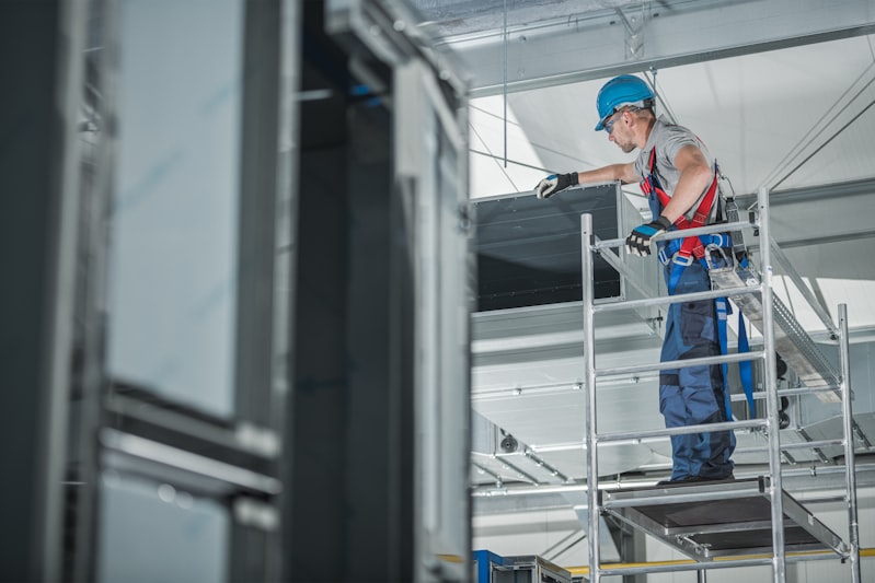 Technician on scaffold inspecting ceiling air ventilation duct in commercial building