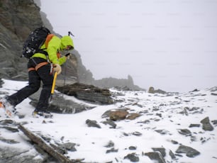 Un alpiniste grimpe une pente raide de neige et de rochers par mauvais temps dans les hautes Alpes suisses