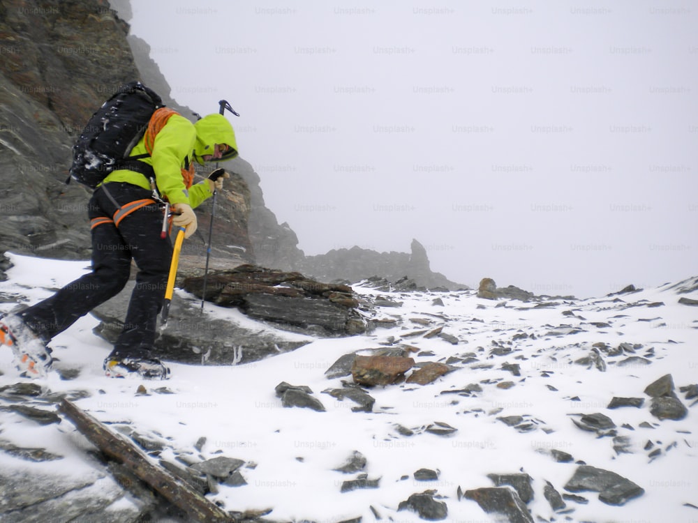 Ein männlicher Bergsteiger auf einem steilen Schnee- und Felshang bei schlechtem Wetter in den Hochalpen der Schweiz