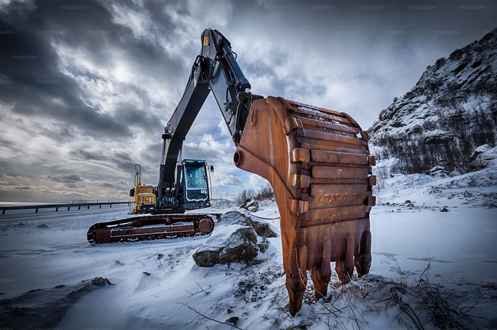 Old excavator with excavator bucket in winter. Road construction in snow. Lofoten islands, Norway. High dynamic range HDR image