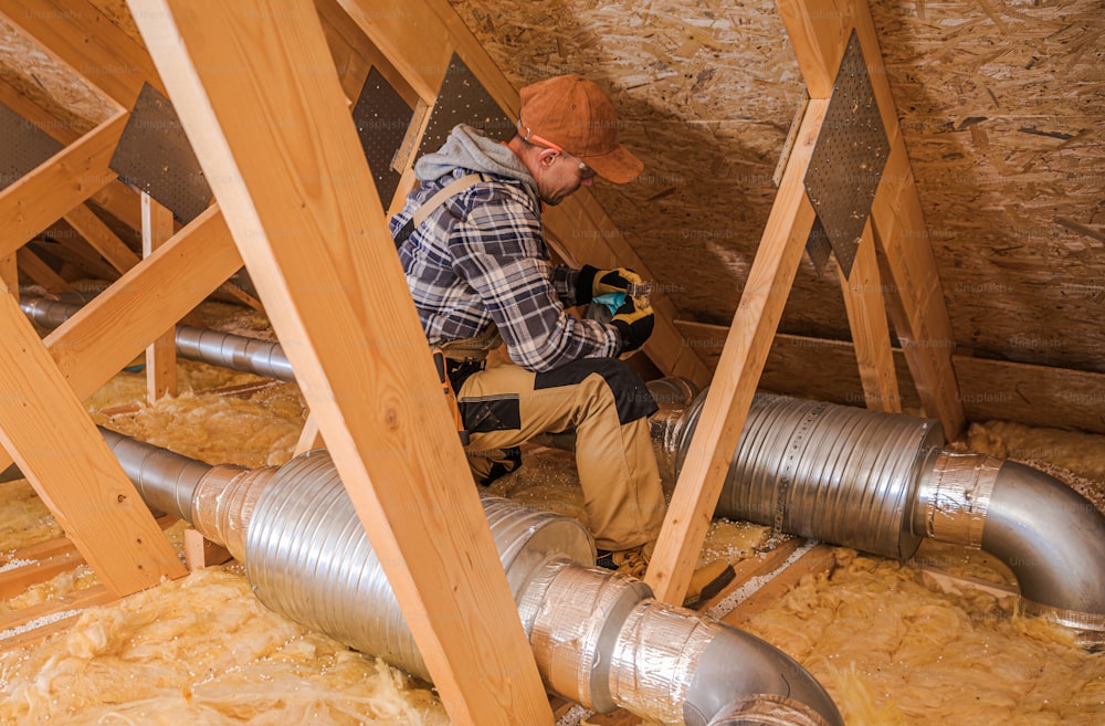 Caucasian HVAC Heating and Cooling Technician in His 40s Installing System Elements in the Home Attic.