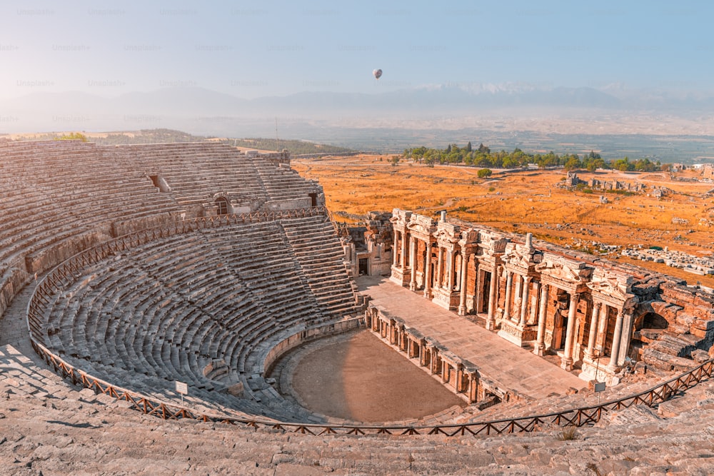 トルコのパムッカレ近郊のヒエラポリス市にある古代ギリシャの円形劇場。驚異と旅行のアトラクション。朝の空に浮かぶ熱気球