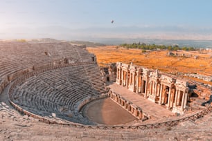 Ancient Greek amphitheater in the city of Hierapolis near Pamukkale in Turkey. Wonders and travel attractions. Hot air balloon above in the morning sky