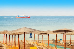 Tropical beach with sunbeds and ferry ship in distance