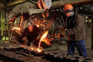 Workers in helmets working in team they melting iron in metal factory