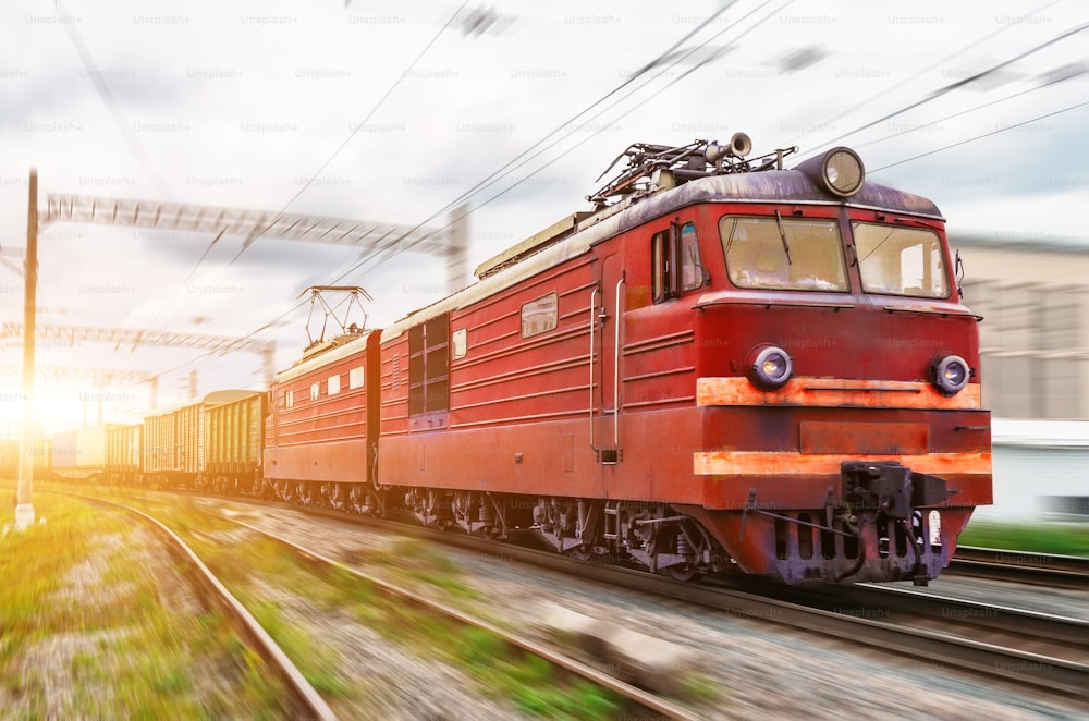 Red locomotive electric with a freight train at high speed rides by rail