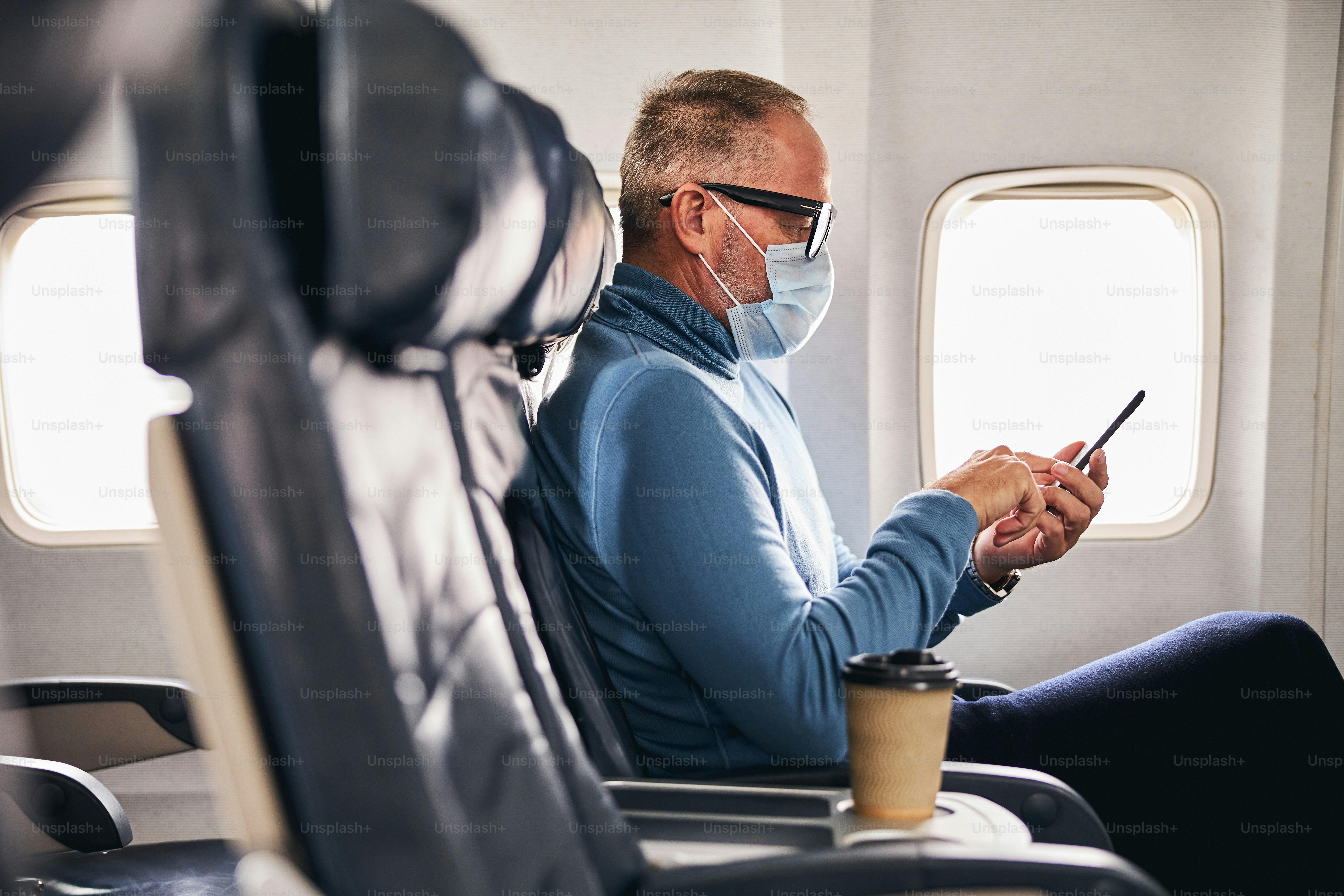 Vue latérale d’un passager masculin sérieux en train d’envoyer des textos sur son téléphone cellulaire pendant le vol