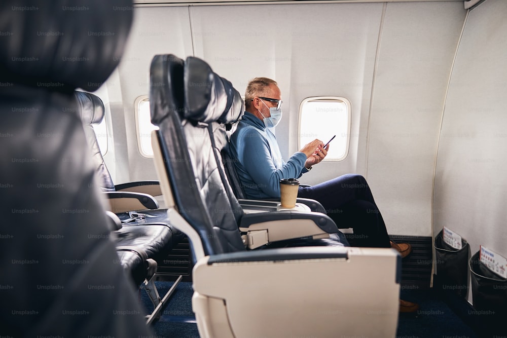 Seitenansicht eines konzentrierten männlichen Passagiers, der in der Flugzeugkabine auf sein Smartphone starrt