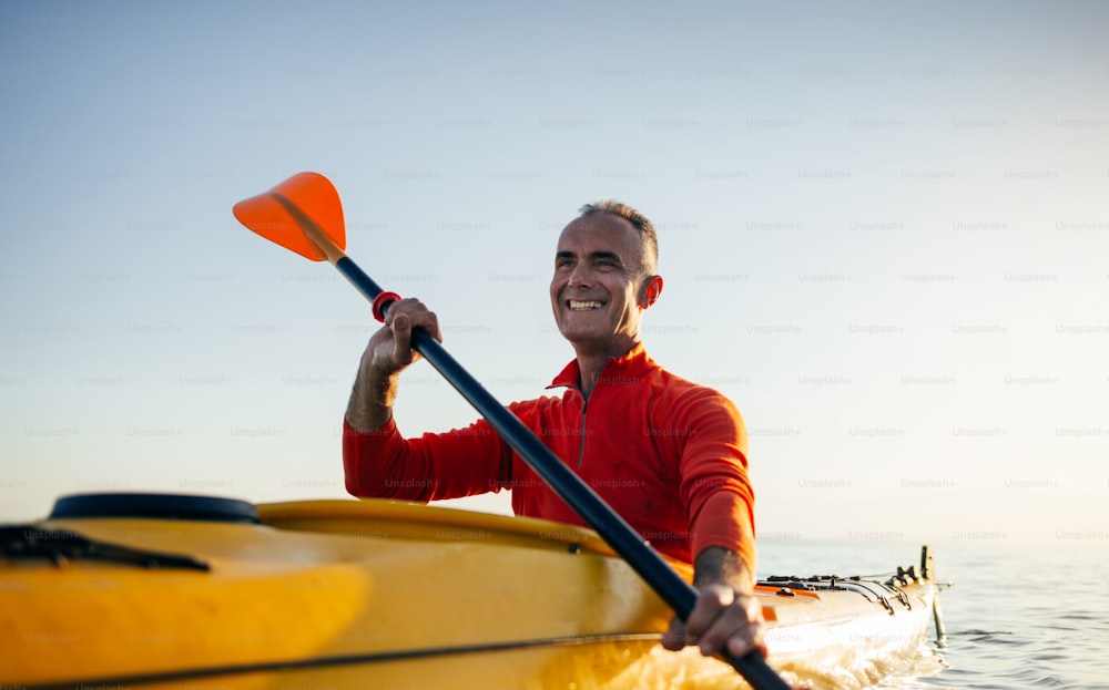Smiling active senior man paddling kayak.