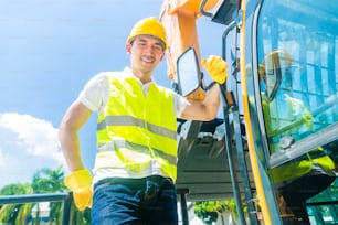 Asian driver standing on construction machinery on building site
