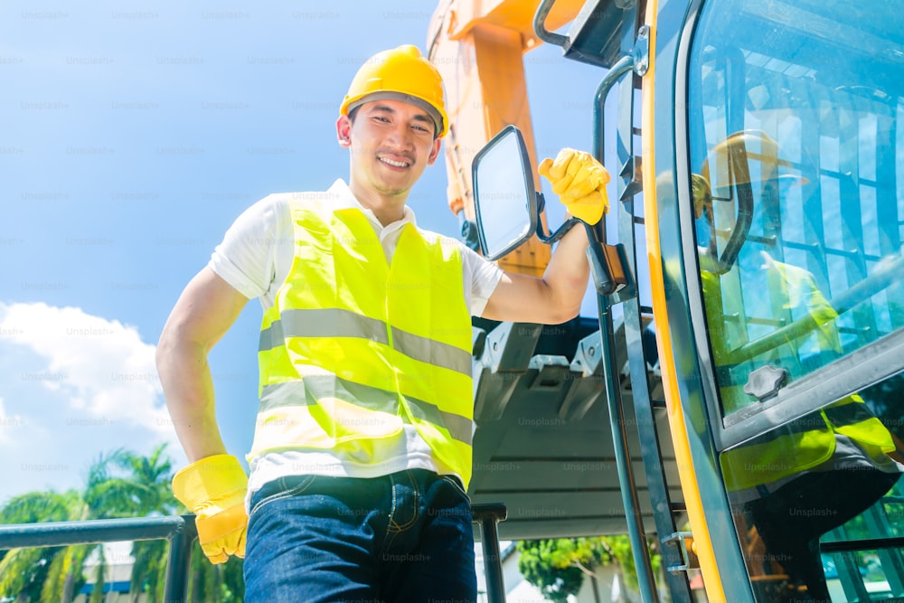 Asian driver standing on construction machinery on building site