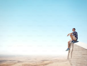 Young man sitting on a top of the cliff and looking at the desert